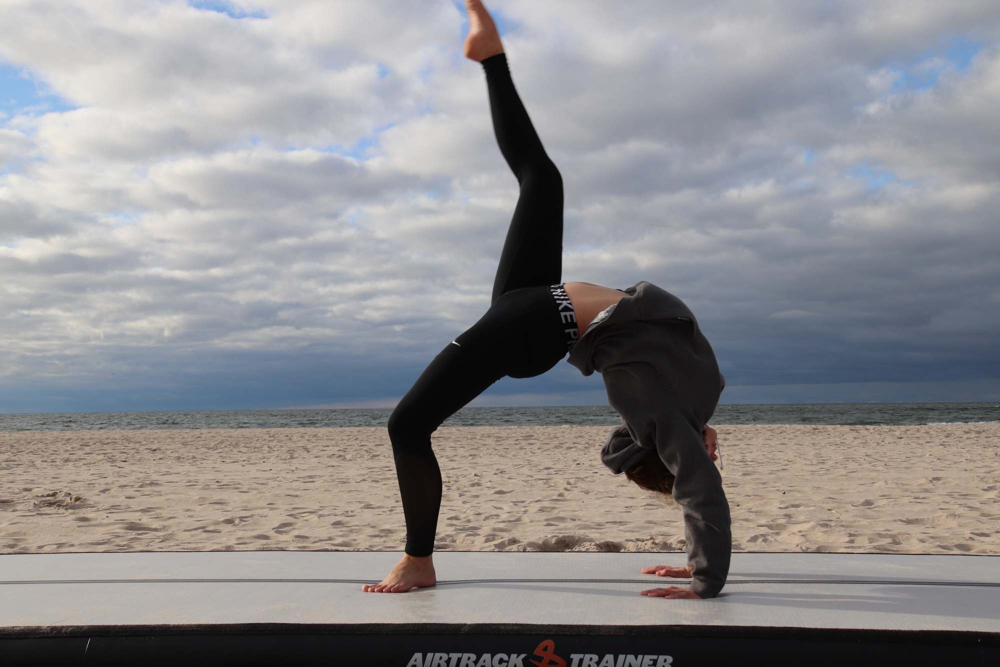Ung gymnast i bro på en airtrack på stranden under en tung skyhimmel
