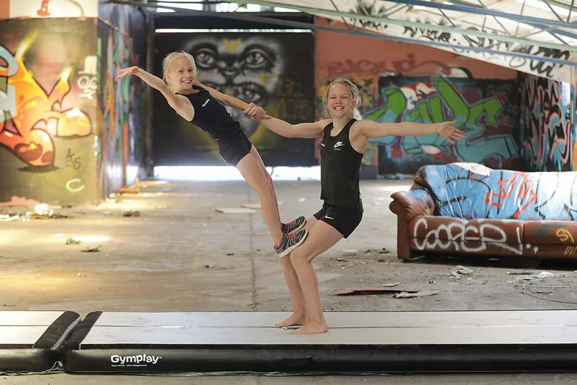 To piger balancerer sammen på en sort airtrack i en graffitimalet hal